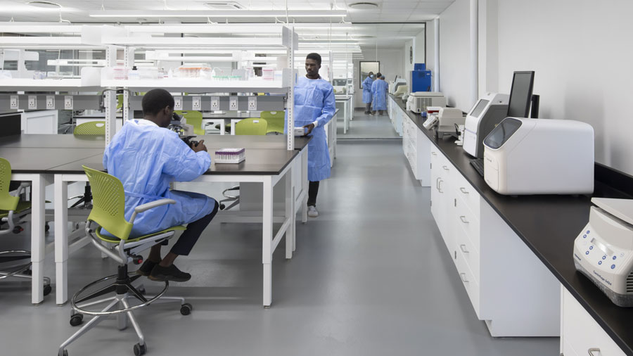 A modern laboratory with two individuals in blue lab coats working at benches with scientific equipment.